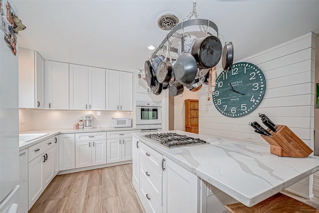 kitchen with light wood-type flooring, stainless steel gas stovetop, backsplash, light stone counters, and white cabinets