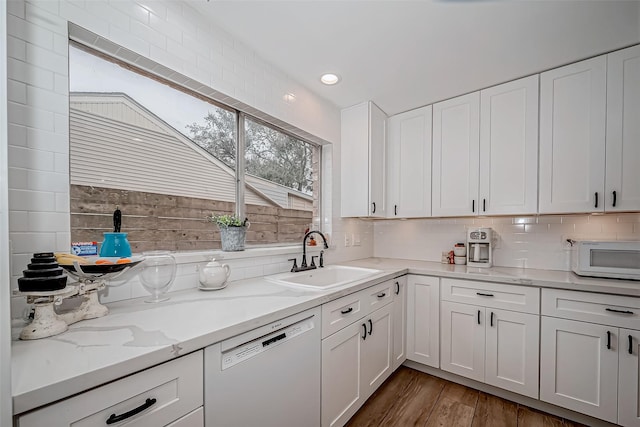 kitchen with tasteful backsplash, light stone counters, dishwashing machine, white cabinets, and sink