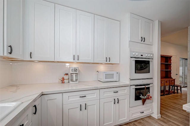 kitchen featuring white appliances, sink, light wood-type flooring, white cabinetry, and tasteful backsplash