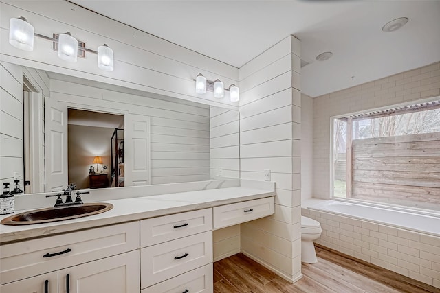 bathroom with hardwood / wood-style flooring, vanity, tiled tub, and toilet