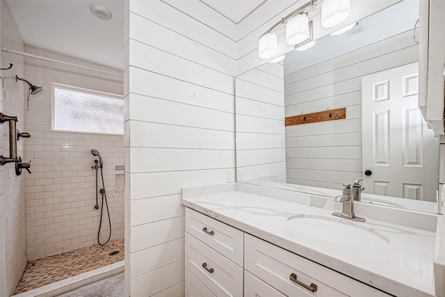 bathroom featuring a tile shower, wood walls, and vanity