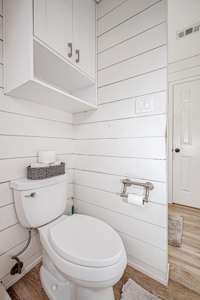 bathroom featuring toilet, hardwood / wood-style flooring, and wooden walls