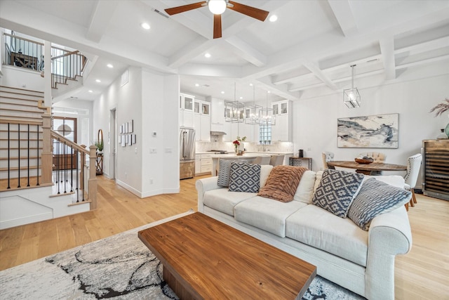 living room with beam ceiling, light wood finished floors, visible vents, baseboards, and stairs