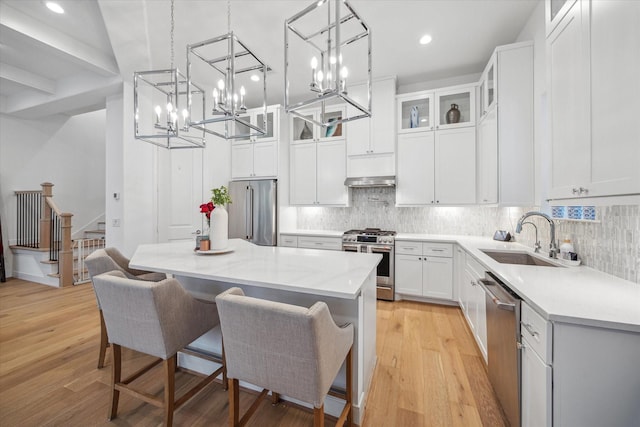 kitchen featuring a kitchen island, glass insert cabinets, appliances with stainless steel finishes, white cabinetry, and a sink