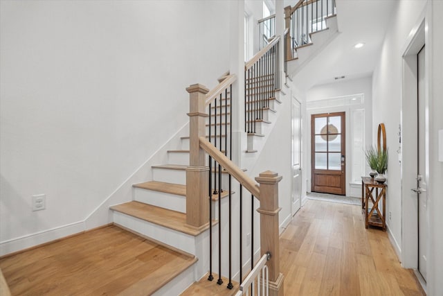 entryway featuring light wood finished floors, baseboards, a towering ceiling, stairs, and recessed lighting