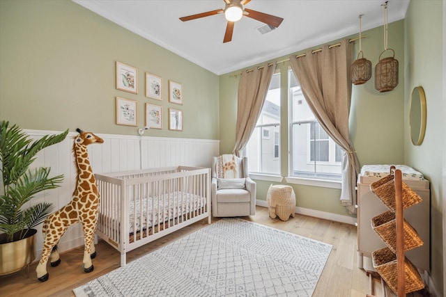 bedroom with visible vents, light wood-type flooring, wainscoting, heating unit, and a crib