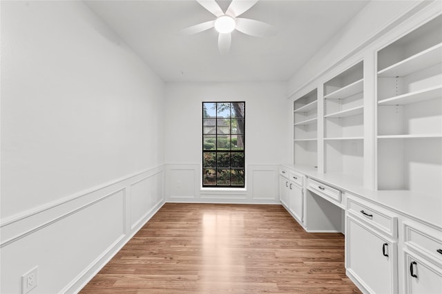 unfurnished office with ceiling fan, light hardwood / wood-style flooring, built in desk, and built in shelves