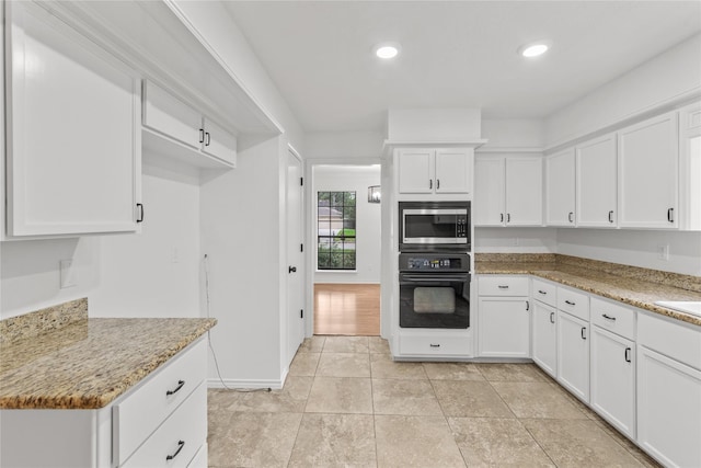 kitchen featuring light stone counters, white cabinets, stainless steel microwave, light tile patterned floors, and black oven