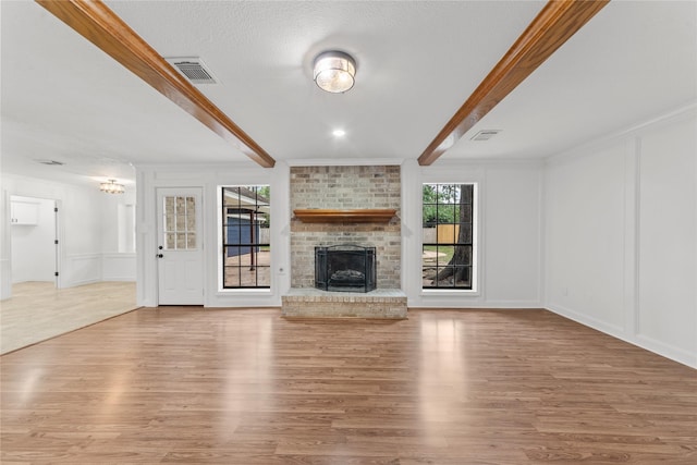 unfurnished living room featuring a fireplace, beamed ceiling, crown molding, and light hardwood / wood-style flooring