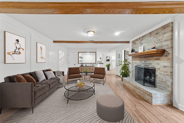 living room with a fireplace, crown molding, light wood-type flooring, and beam ceiling