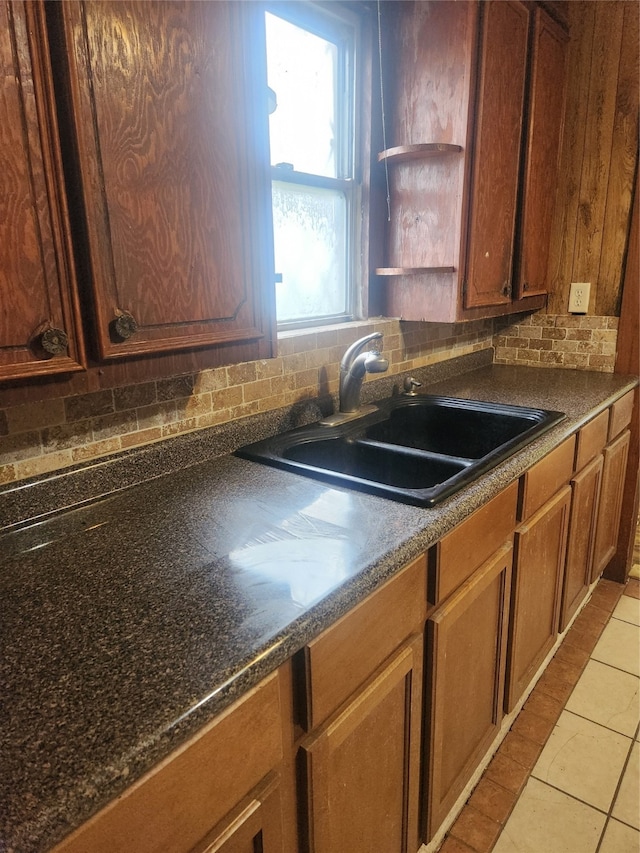 kitchen featuring brown cabinets, open shelves, tasteful backsplash, dark countertops, and a sink