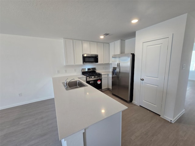 kitchen featuring a sink, wood finished floors, stainless steel appliances, white cabinets, and light countertops