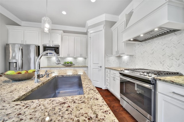 kitchen with white cabinets, appliances with stainless steel finishes, premium range hood, pendant lighting, and a sink