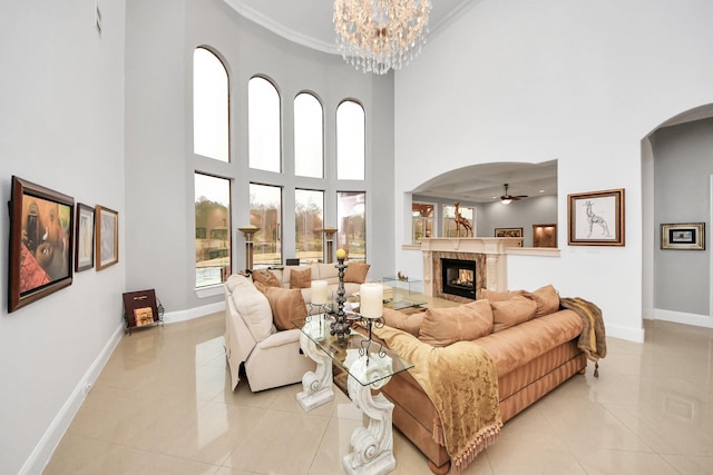 living room featuring light tile patterned floors, a towering ceiling, a tiled fireplace, ceiling fan with notable chandelier, and ornamental molding