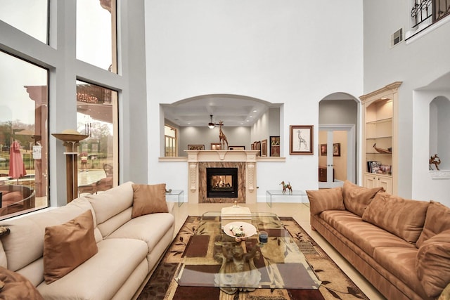 living room featuring a towering ceiling, built in shelves, ceiling fan, and a premium fireplace