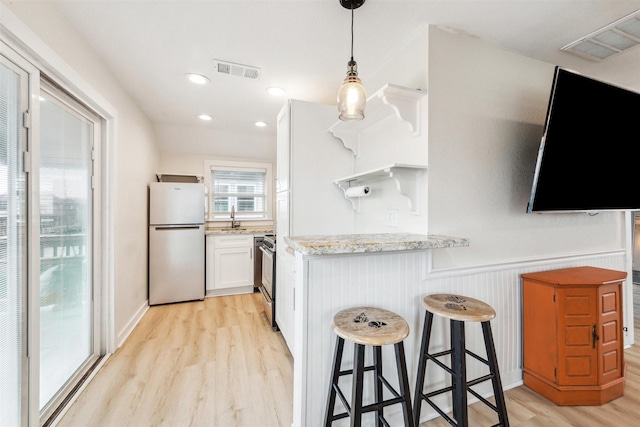 kitchen with light stone countertops, visible vents, white cabinets, and freestanding refrigerator