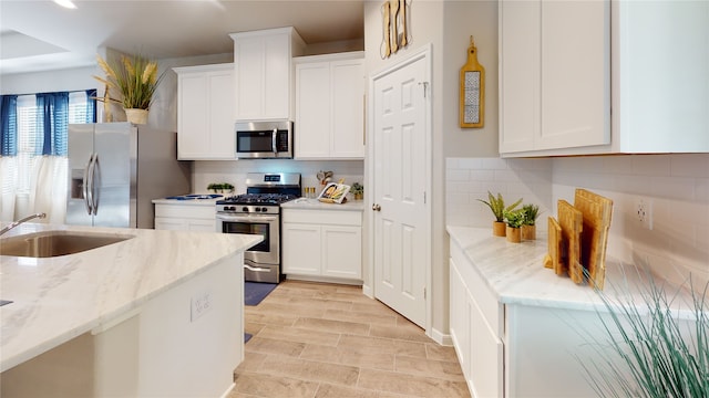 kitchen featuring stainless steel appliances, light stone countertops, sink, tasteful backsplash, and white cabinets