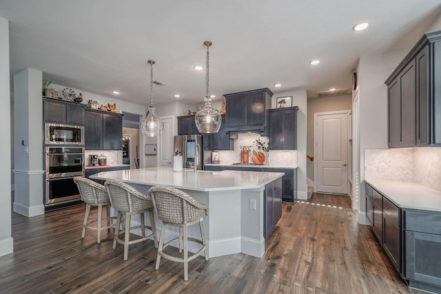 kitchen featuring dark wood-style floors, stainless steel appliances, a large island with sink, and light countertops