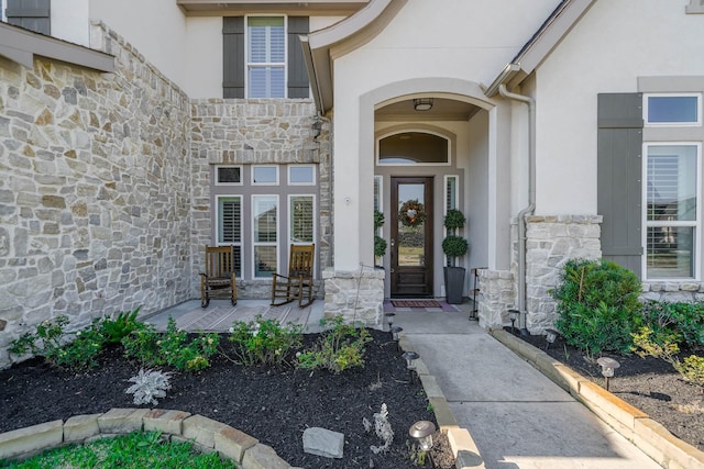 entrance to property featuring a porch, stone siding, and stucco siding