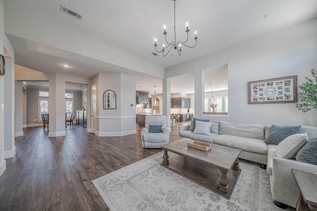 living area with an inviting chandelier, baseboards, visible vents, and dark wood finished floors