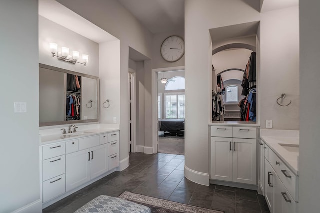 bathroom with baseboards, a ceiling fan, a sink, a walk in closet, and two vanities