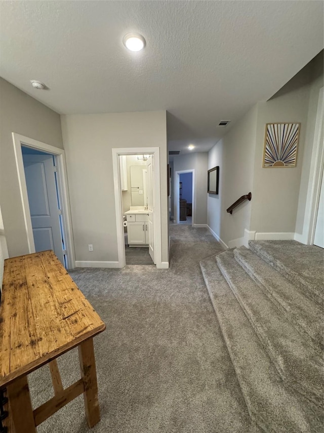 hall with a textured ceiling, visible vents, baseboards, stairway, and dark colored carpet