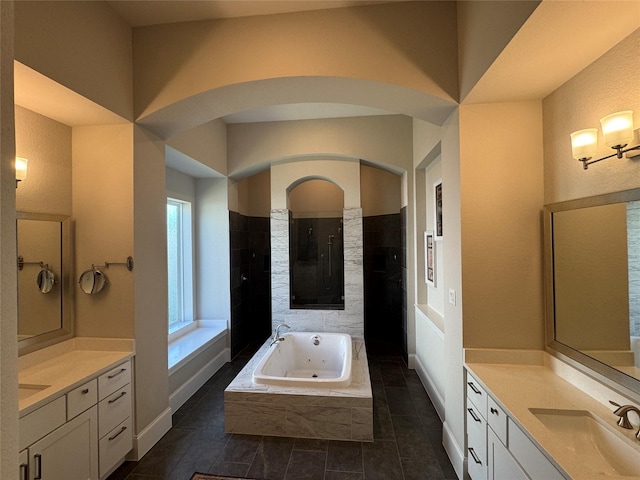 bathroom featuring tiled shower, a jetted tub, two vanities, and a sink