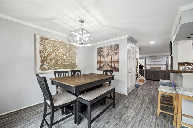 dining space with a chandelier, a fireplace, wood finished floors, baseboards, and crown molding