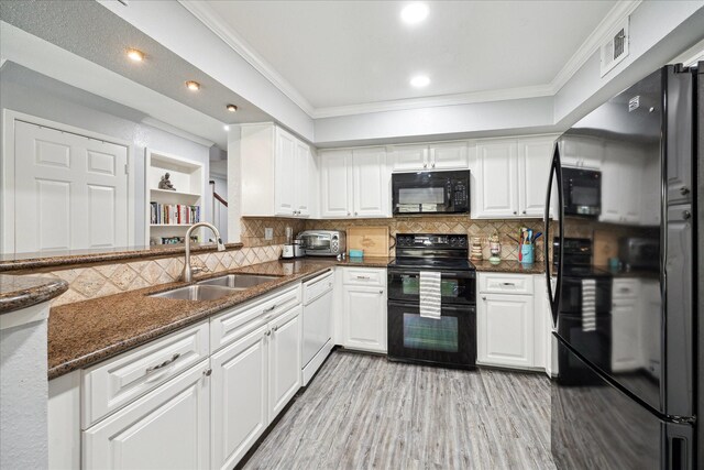 kitchen with black appliances, a sink, white cabinetry, crown molding, and dark stone countertops