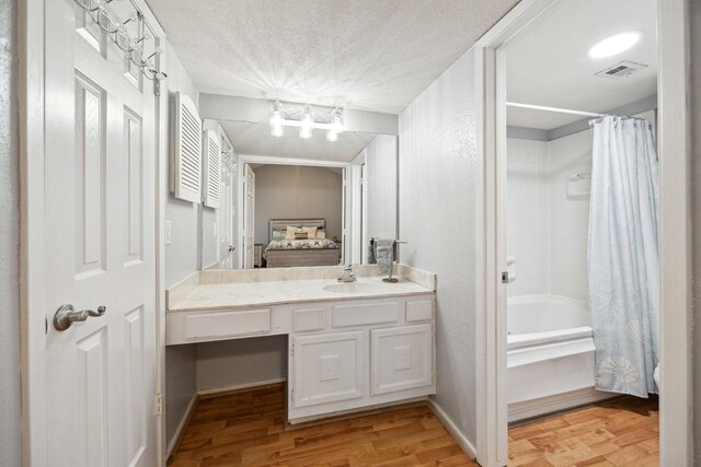 ensuite bathroom featuring wood finished floors, vanity, shower / bath combination with curtain, a chandelier, and a textured ceiling