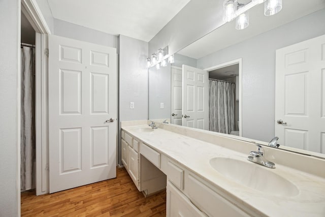 bathroom with a sink, double vanity, toilet, and wood finished floors