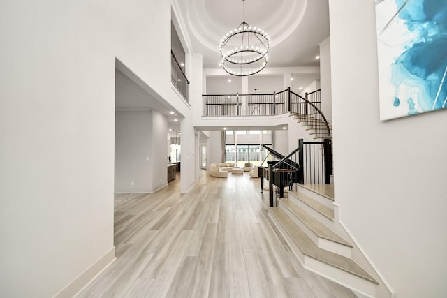 foyer entrance featuring a tray ceiling, a high ceiling, a chandelier, and light hardwood / wood-style flooring