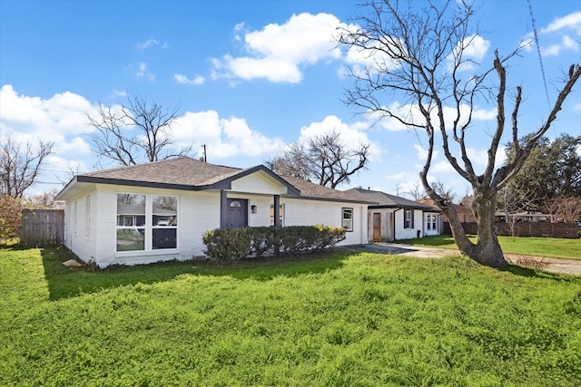 ranch-style home with a shingled roof, a front yard, brick siding, and fence