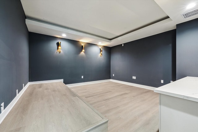 spare room featuring a tray ceiling and light wood-type flooring