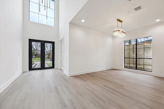 entryway featuring a notable chandelier, plenty of natural light, a towering ceiling, and light hardwood / wood-style flooring