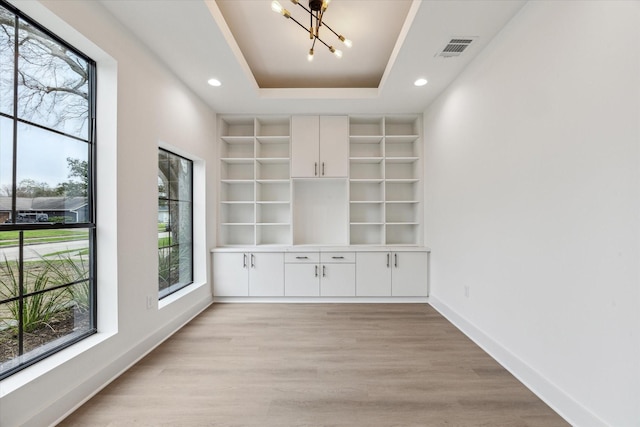 interior space with a tray ceiling, built in shelves, a chandelier, and light hardwood / wood-style flooring