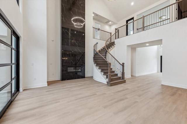 interior space featuring a notable chandelier, a premium fireplace, light wood-type flooring, and a high ceiling