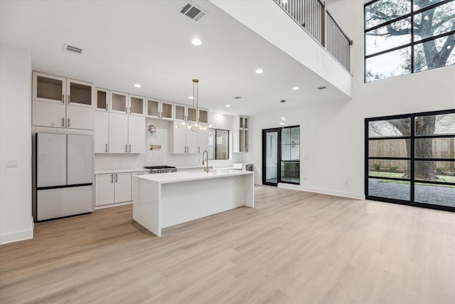 kitchen with decorative light fixtures, paneled refrigerator, light hardwood / wood-style floors, white cabinets, and a kitchen island with sink