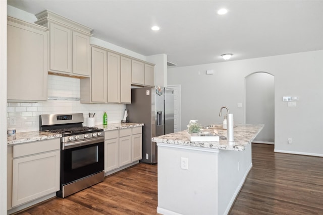 kitchen with an island with sink, stainless steel appliances, light stone countertops, dark hardwood / wood-style floors, and decorative backsplash