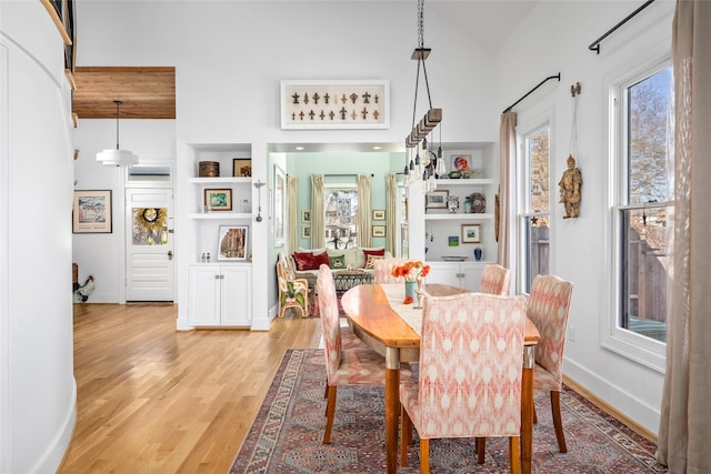 dining space featuring built in features, light wood-style floors, baseboards, and high vaulted ceiling