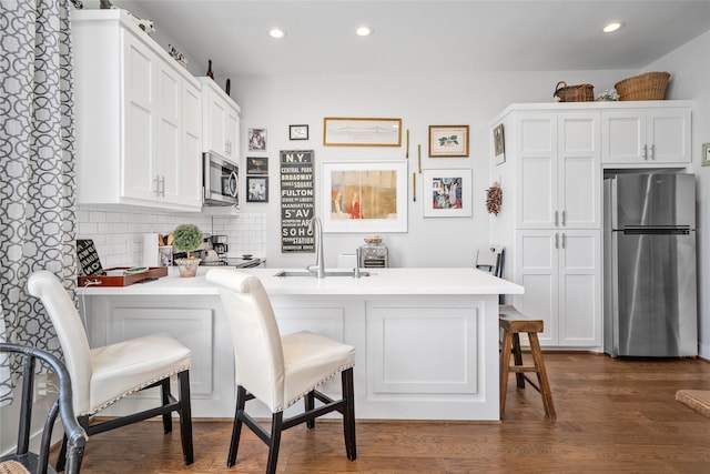 kitchen with a kitchen bar, appliances with stainless steel finishes, a peninsula, white cabinets, and decorative backsplash