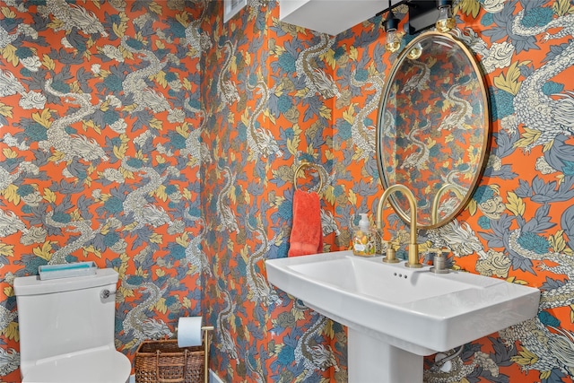 half bathroom with a sink, toilet, and wallpapered walls