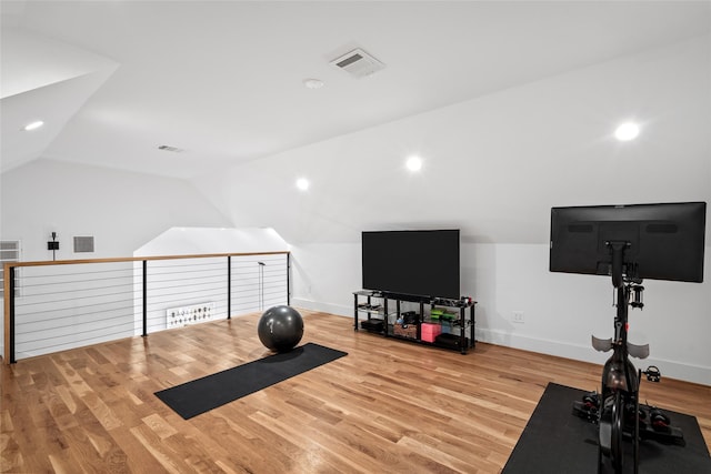 exercise room with vaulted ceiling, wood finished floors, visible vents, and baseboards