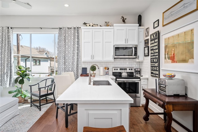 kitchen with a sink, backsplash, appliances with stainless steel finishes, white cabinets, and dark wood-style flooring