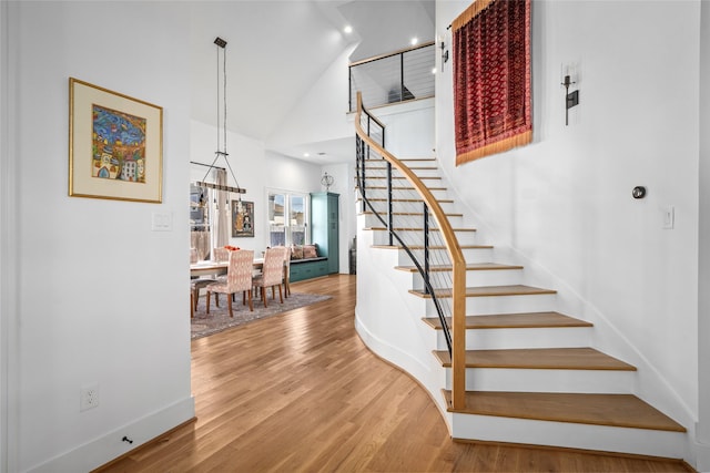 stairway featuring baseboards, high vaulted ceiling, and wood finished floors