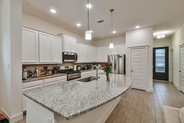 kitchen featuring appliances with stainless steel finishes, an island with sink, pendant lighting, sink, and white cabinetry