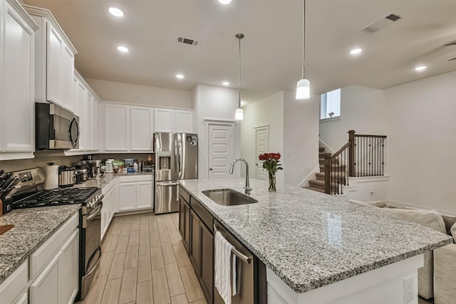 kitchen with appliances with stainless steel finishes, sink, white cabinets, hanging light fixtures, and a kitchen island with sink