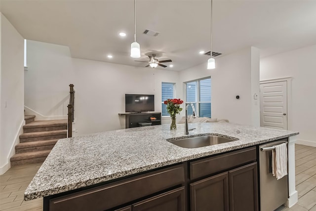 kitchen with an island with sink, sink, stainless steel dishwasher, dark brown cabinets, and light stone counters