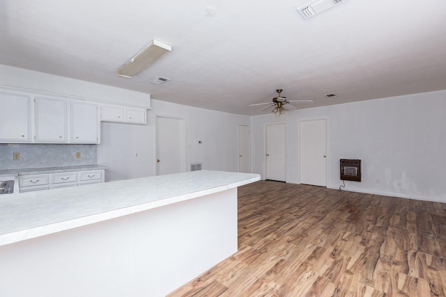 kitchen featuring tasteful backsplash, white cabinets, ceiling fan, light wood-type flooring, and heating unit