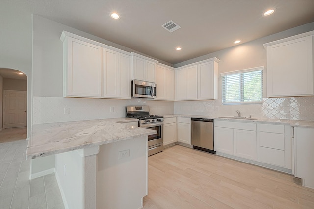 kitchen with appliances with stainless steel finishes, white cabinetry, light stone countertops, and sink